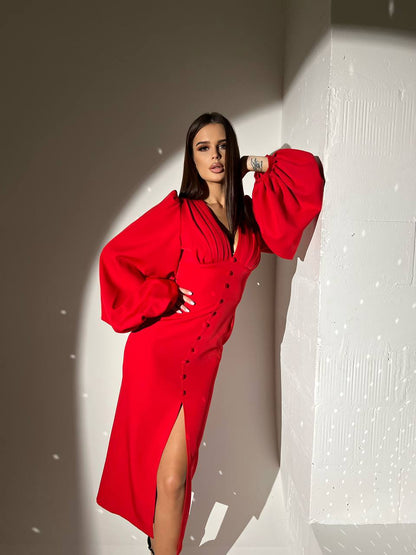 Woman in a red dress posing against a textured wall.