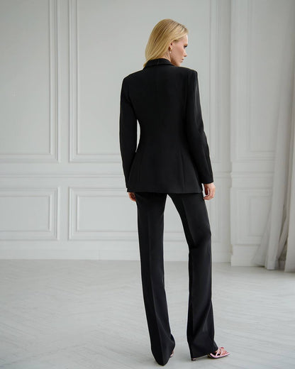 Woman wearing a black suit standing in a room with white walls and light gray floor.