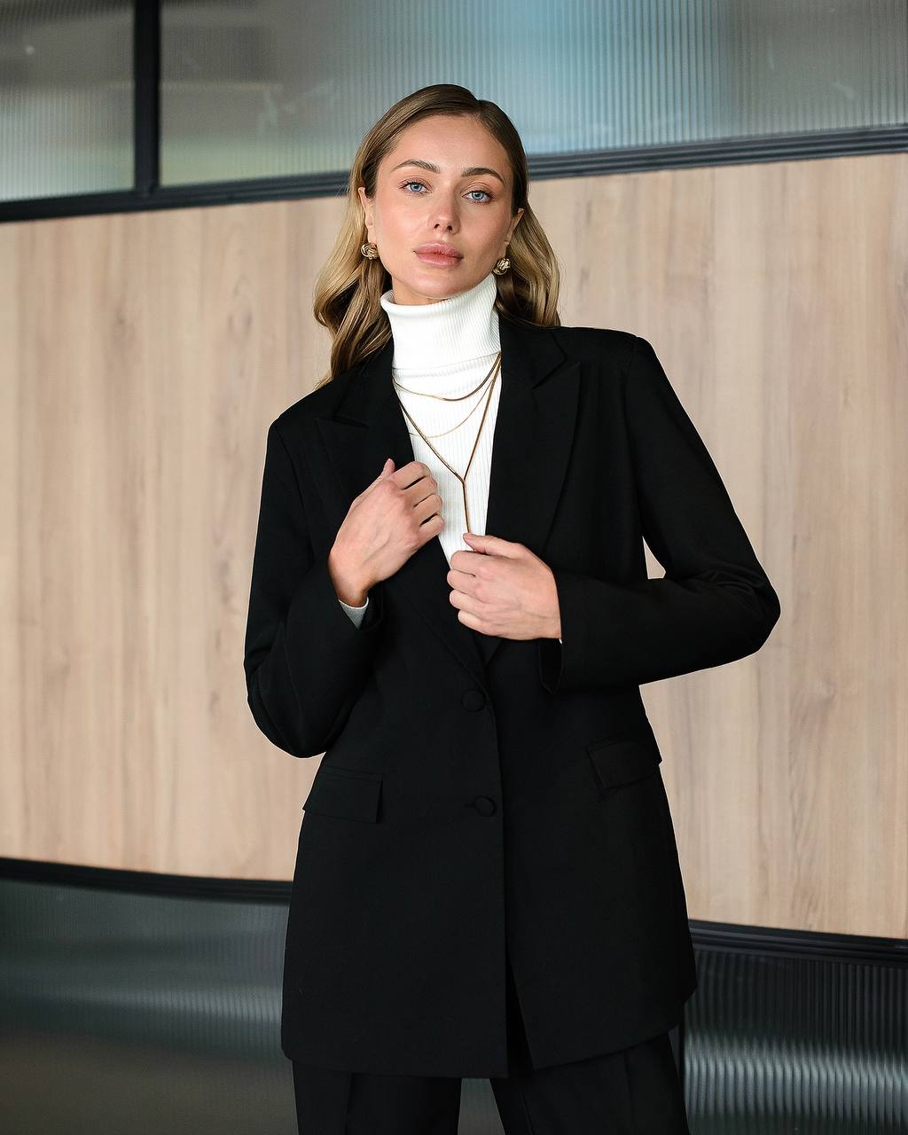 Woman wearing a black suit with a white turtleneck against a wooden panel background