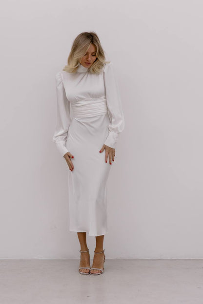 Woman wearing a white dress with long sleeves against a plain background