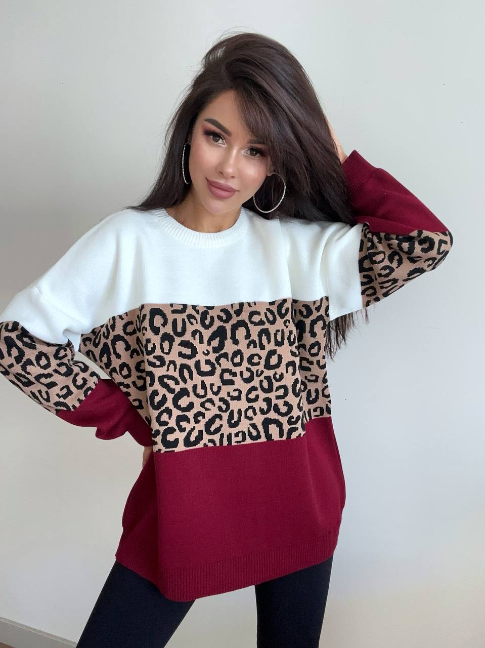Woman wearing a sweater with leopard print and red sleeves against a white background