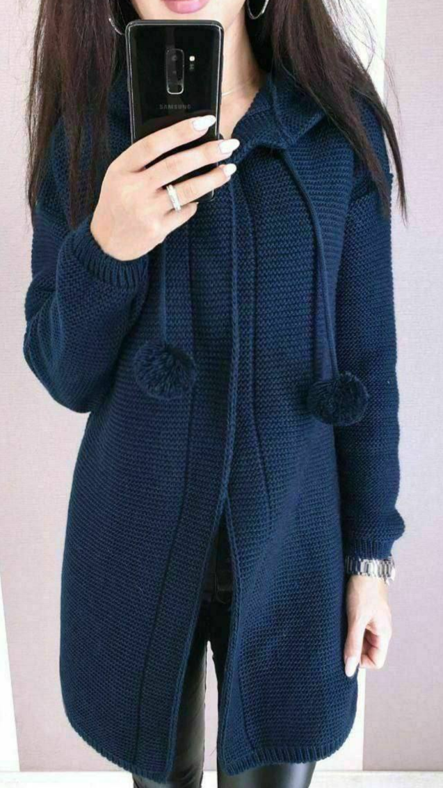 Person wearing a navy blue knitted cardigan with pom-pom details, holding a phone.