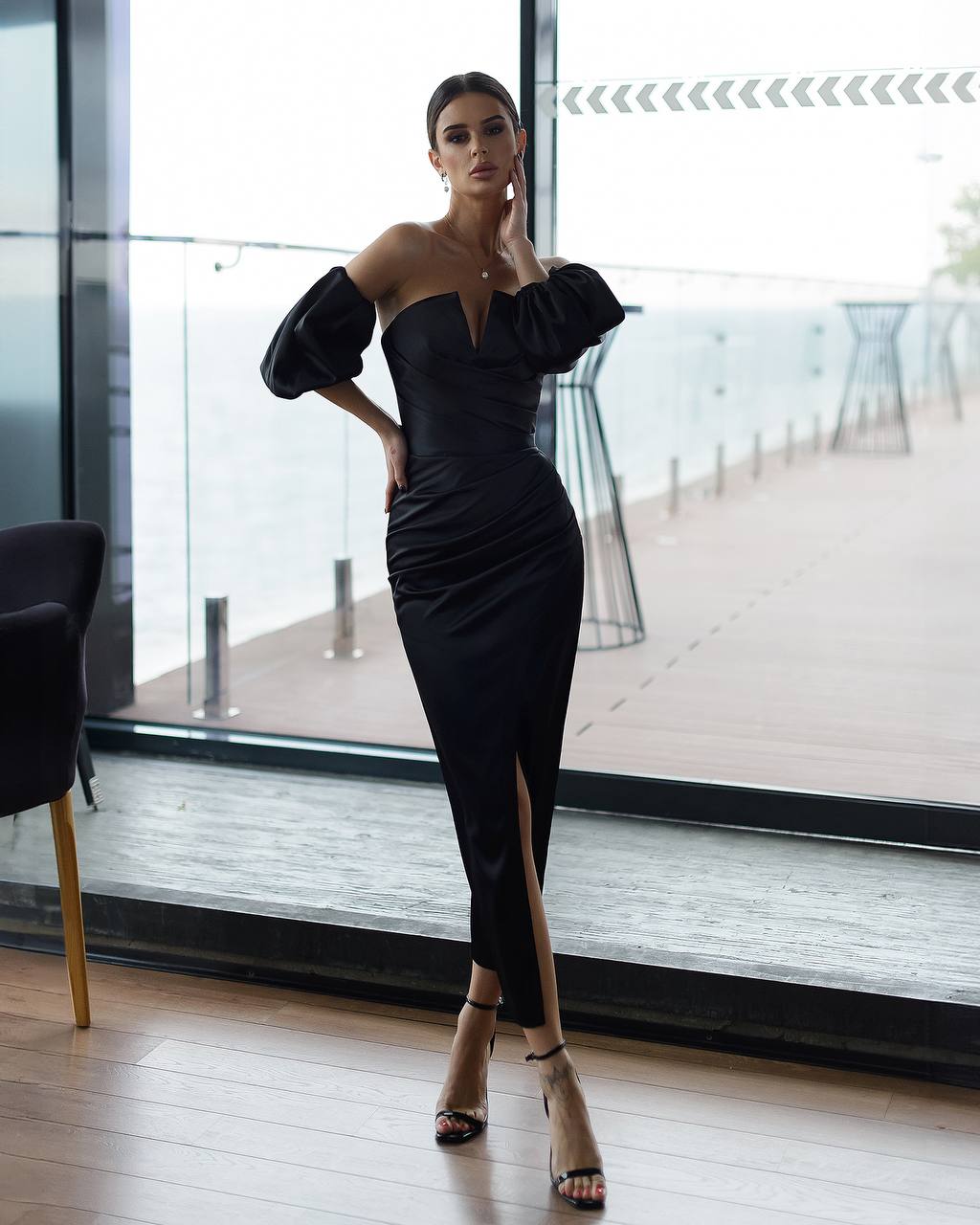 Woman in a black dress standing in a modern indoor setting with large windows.