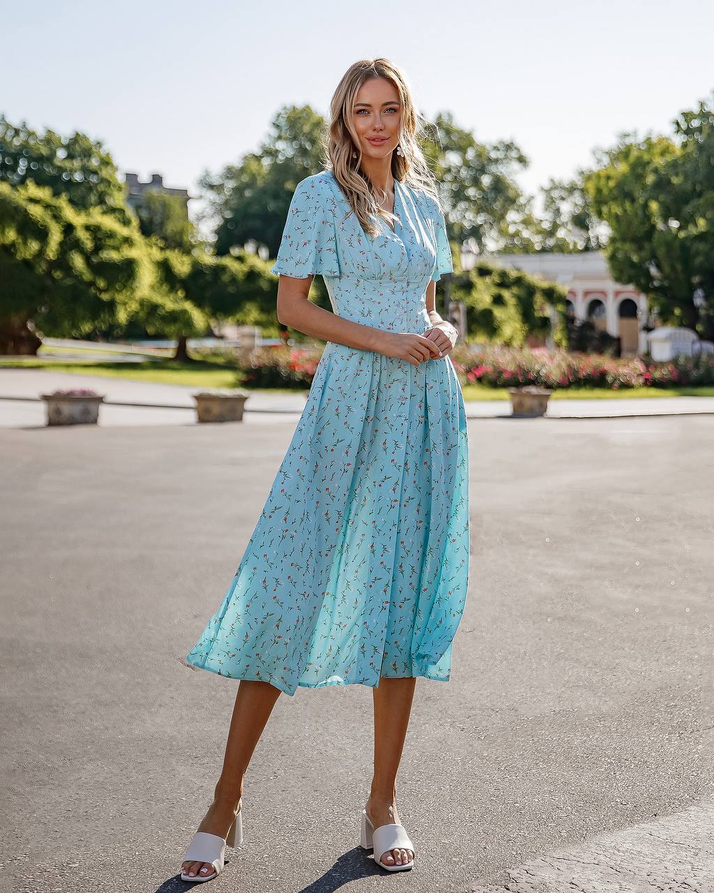 Woman in a light blue dress standing outdoors with greenery in the background