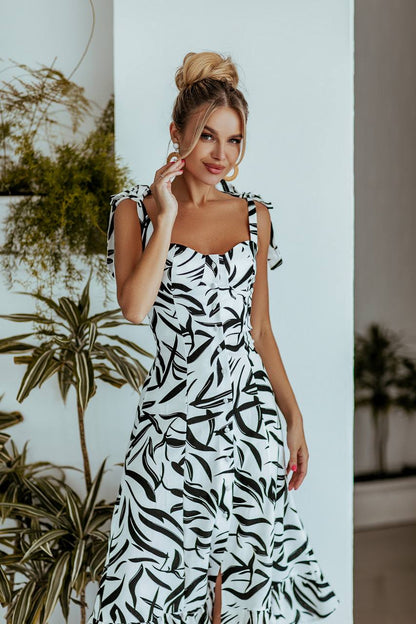 Woman wearing a black and white patterned dress standing indoors with plants in the background