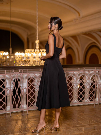 Woman in a black dress standing in an elegant indoor setting with chandeliers.