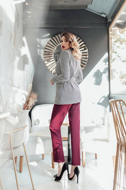 Woman in a stylish outfit with a checkered blazer and red pants standing in a modern interior setting.