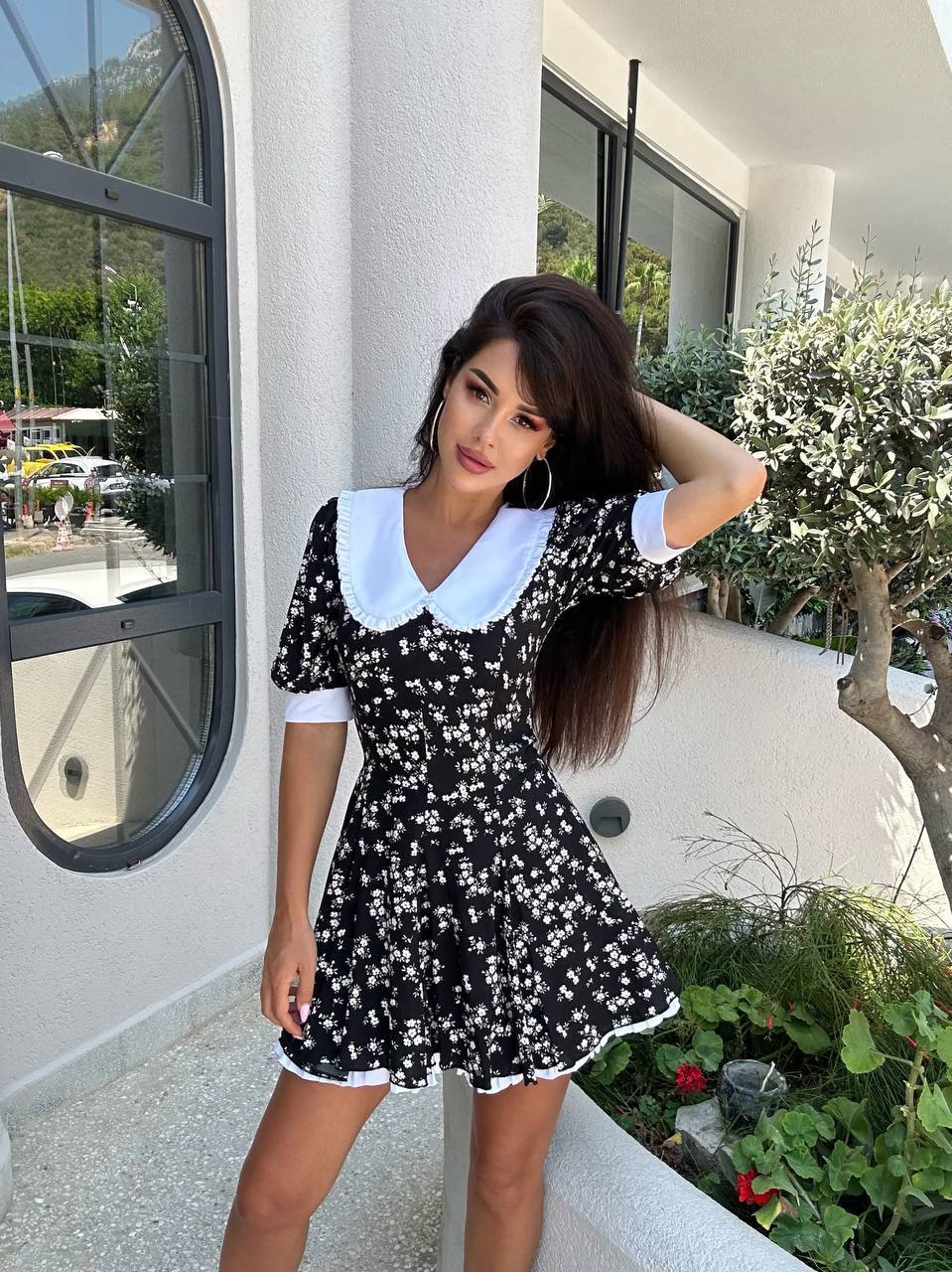 Woman in a black floral dress with white collar standing outdoors.