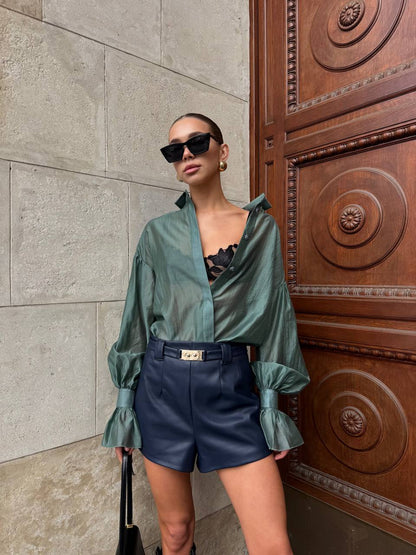 Woman in green shirt and blue shorts standing against a textured wall with a wooden door.