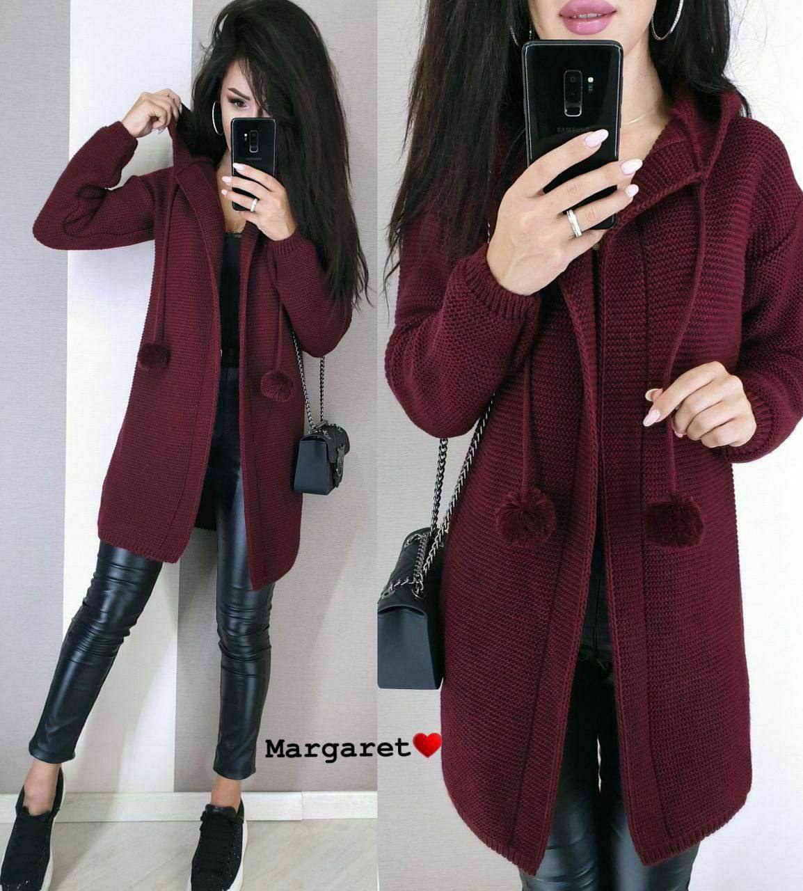Woman wearing a burgundy cardigan with pom-poms, taking a mirror selfie.