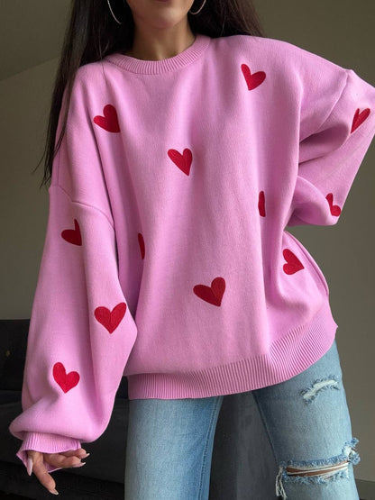 Person wearing a pink sweater with red heart patterns and light blue jeans.