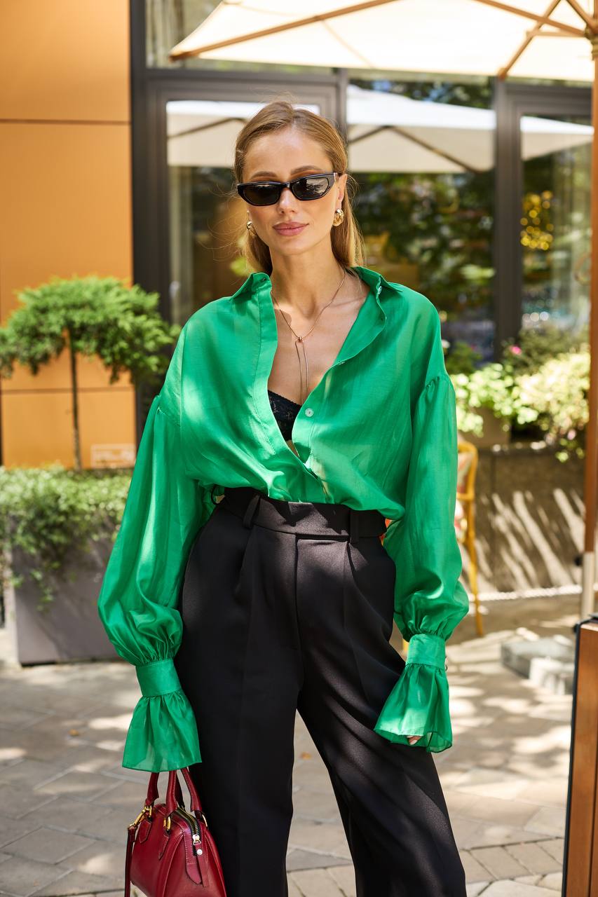 Woman wearing a green blouse and black pants outdoors.