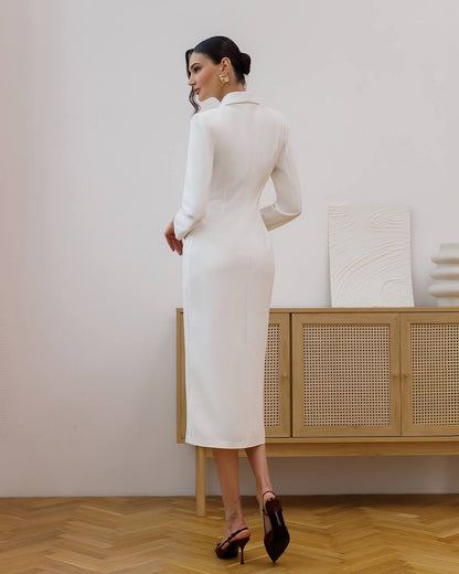 Woman in a white dress standing in a room with wooden flooring and a light-colored wall.