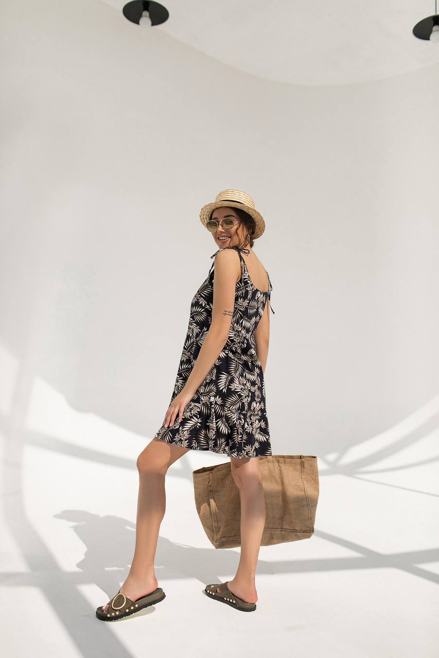 Woman in a black floral dress with a straw hat and bag, standing against a white background
