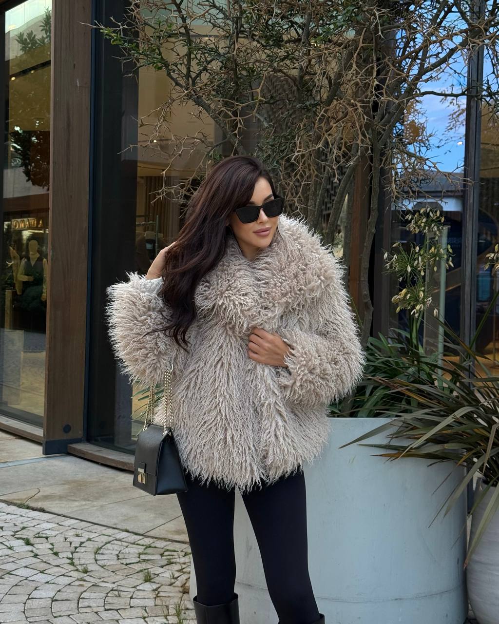 Woman wearing a fluffy beige coat standing outdoors near a building entrance.