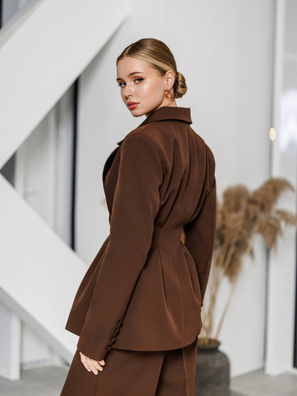 Woman wearing a brown outfit standing in an indoor setting with a neutral background