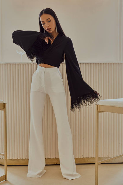 Woman wearing a black top with fringes and white pants in a minimalistic setting
