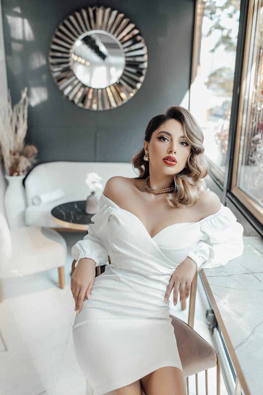 Woman in a white dress sitting in a stylish interior setting.