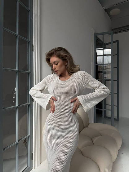 Woman in a white dress standing in a modern room with large windows.