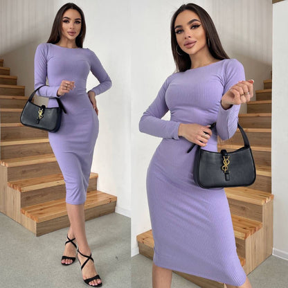 Woman in a purple dress holding a black handbag on wooden stairs.