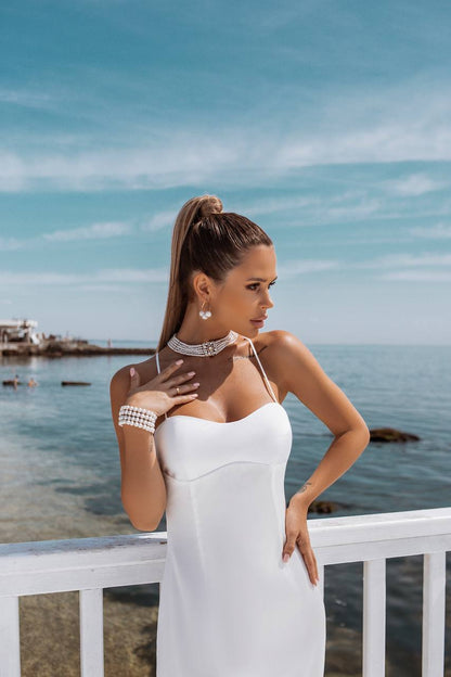 Woman in a white dress standing by a railing with a scenic ocean view.