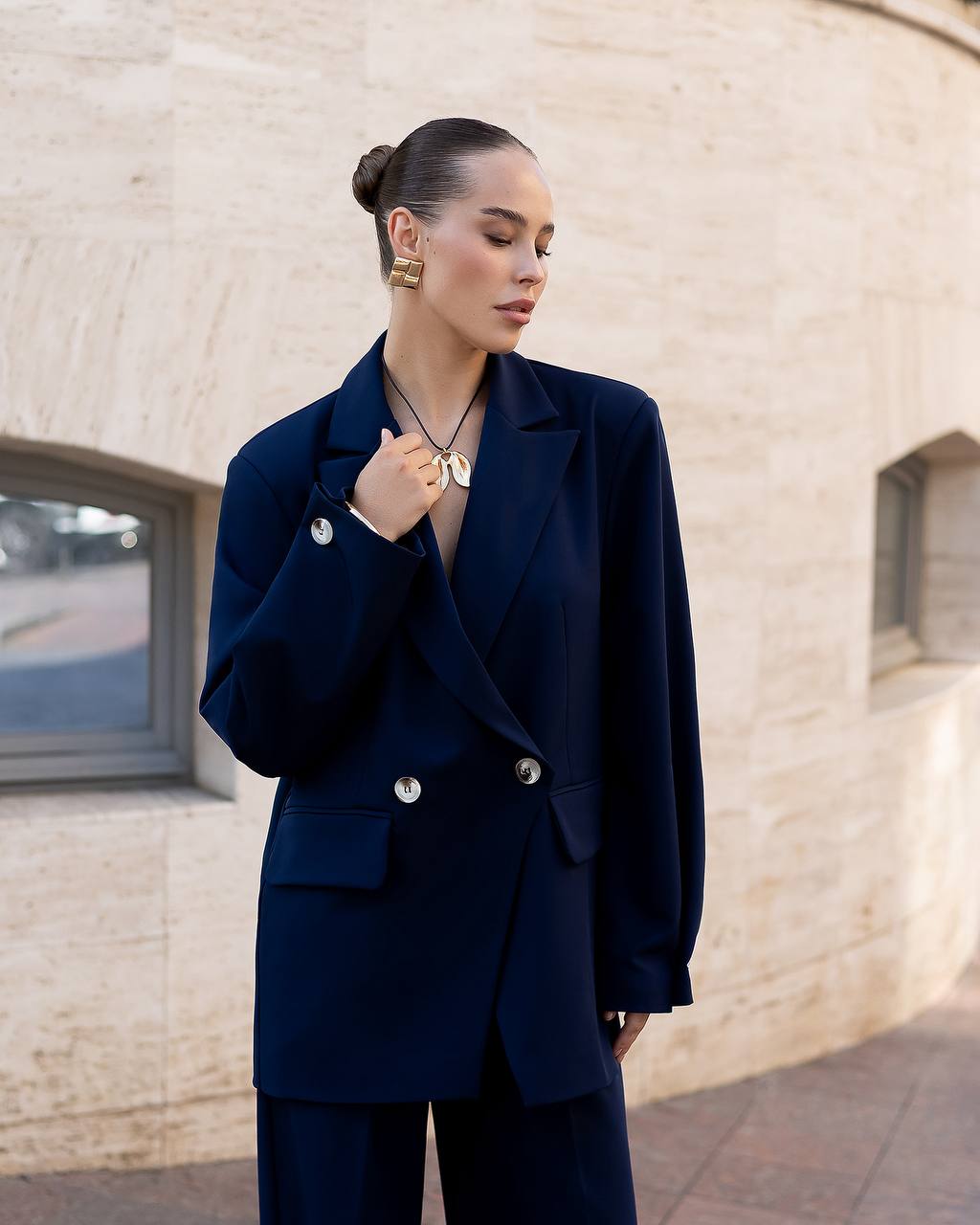 Woman wearing a navy blue suit standing against a light-colored wall.