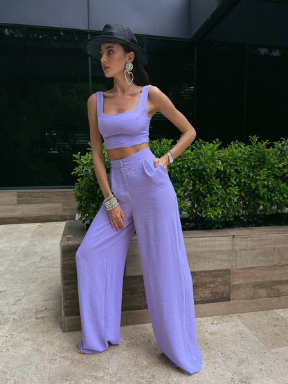 Woman in a lavender outfit standing outdoors with greenery in the background