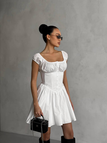 Woman in a white dress holding a black handbag against a gray background