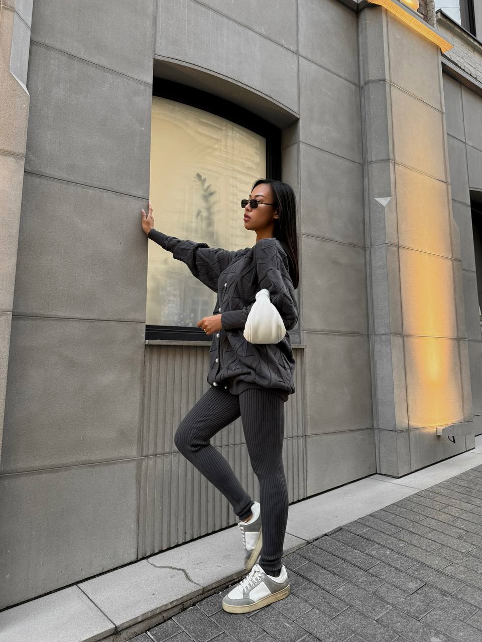 Woman in gray outfit leaning against a building wall