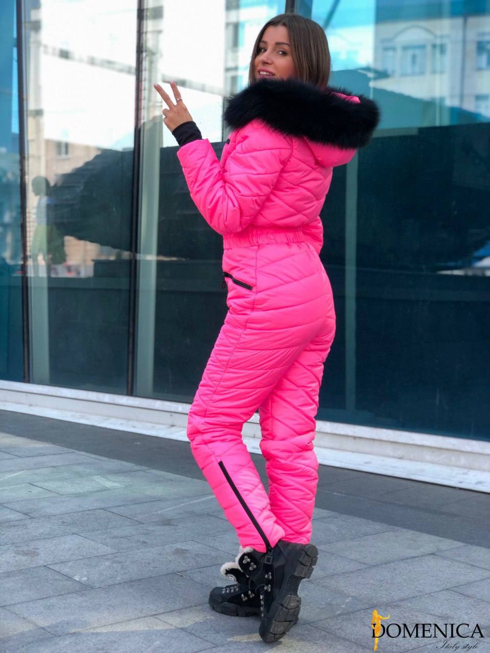 Person wearing a bright pink puffer suit with a black fur hood in an urban setting.