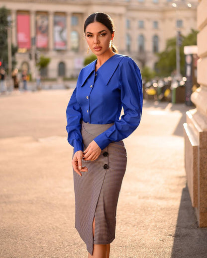 Woman wearing a blue blouse and gray skirt standing on a street with buildings in the background