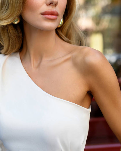 Woman wearing a white one-shoulder top with a blurred background