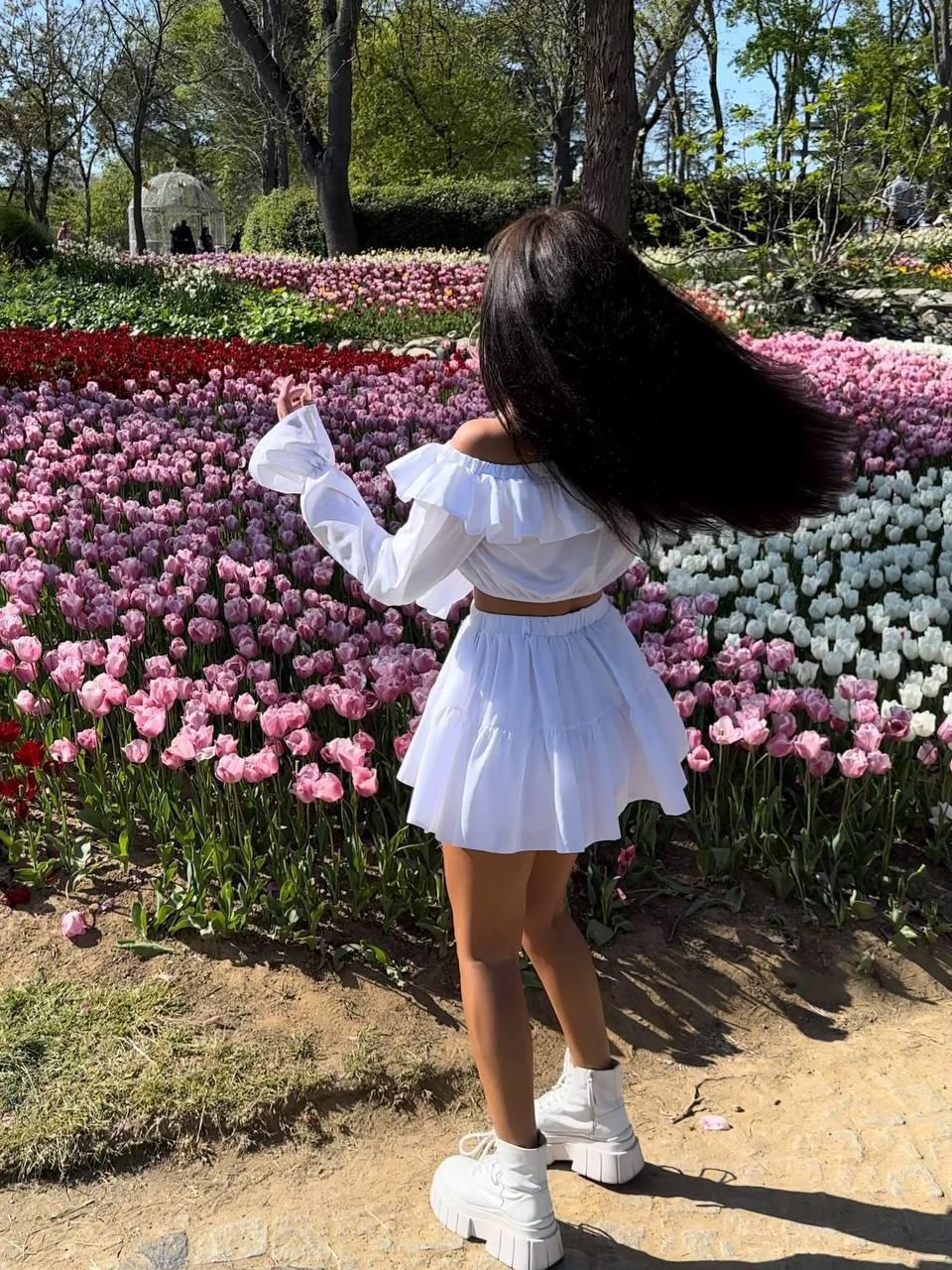 Person in a white outfit standing in front of a colorful flower display