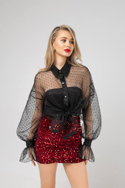 Woman wearing a black sheer top with a red sequin skirt on a gray background