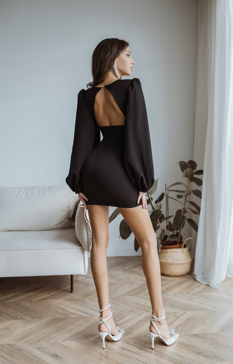 Woman in a black dress standing in a room with a couch and plants.