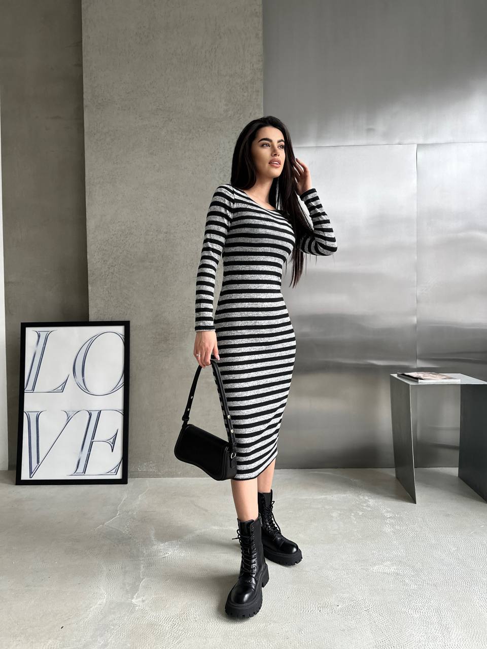 Woman in a black and white striped dress standing in a modern interior setting with 'LOVE' artwork.