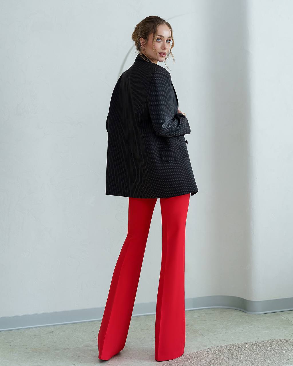 Person wearing a black jacket and red pants against a plain wall.