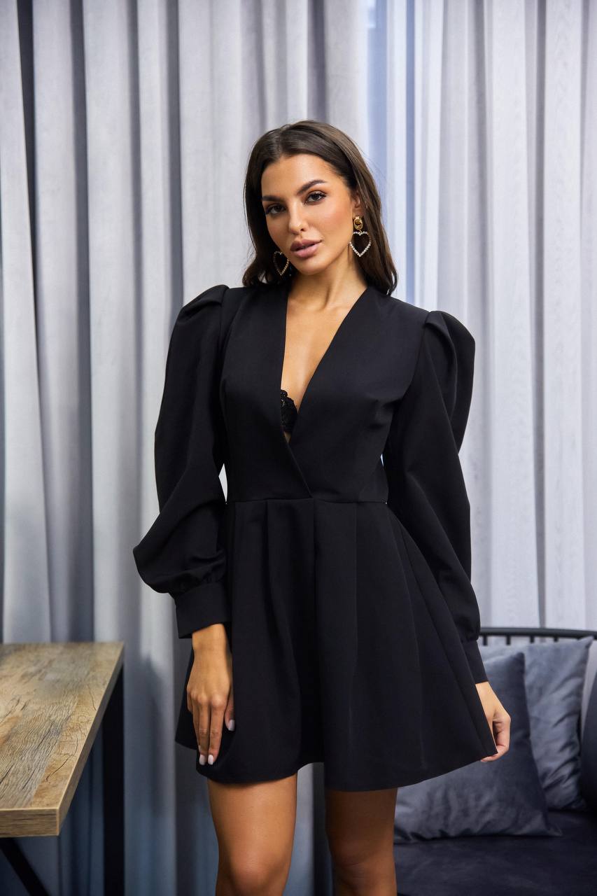 Woman wearing a black dress with puffed sleeves in a room with gray curtains.