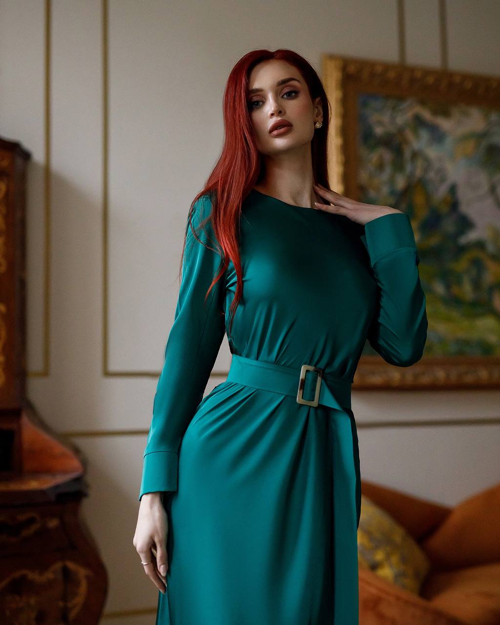 Woman in a teal dress standing in an indoor setting with a painting in the background