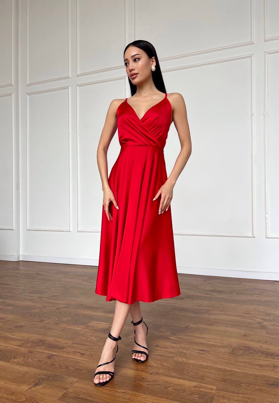 Woman wearing a red dress standing in a room with wooden flooring and white paneled walls.