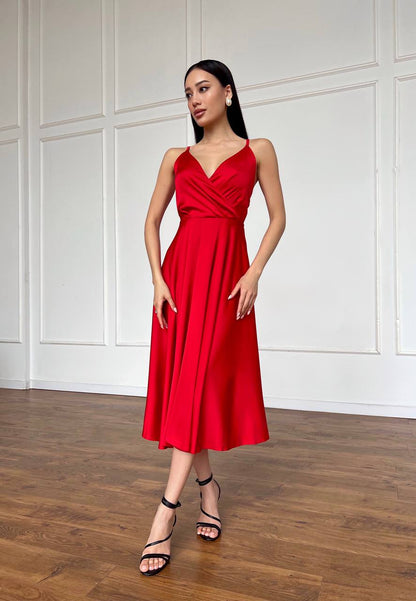 Woman wearing a red dress standing in a room with wooden flooring and white paneled walls.