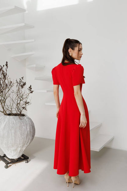 Woman in a red dress standing in a minimalistic room with white walls and a large vase.
