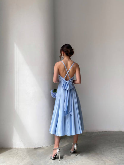 Woman in a light blue dress standing against a plain wall.
