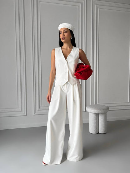 Woman in a white outfit holding a red clutch against a gray wall.