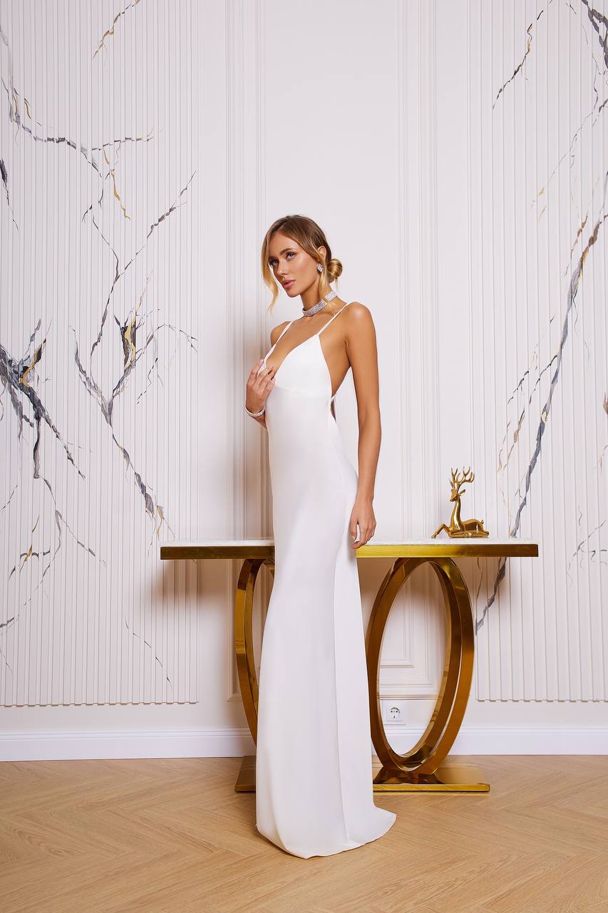 Woman in a white dress standing in a room with marble walls and a gold table.