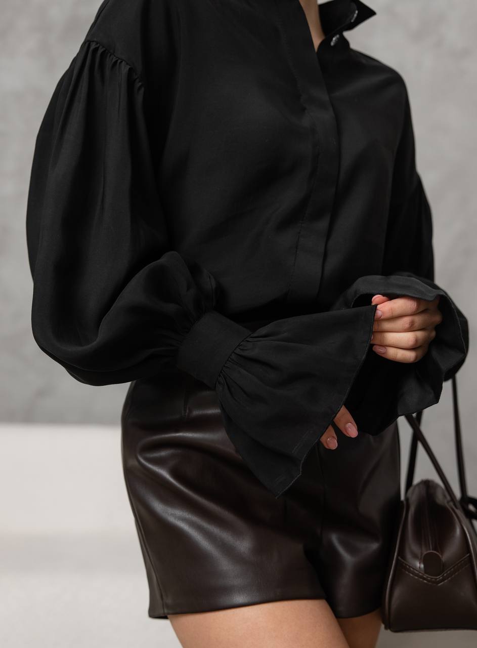 Person wearing a black blouse with puffed sleeves and a leather skirt against a neutral background