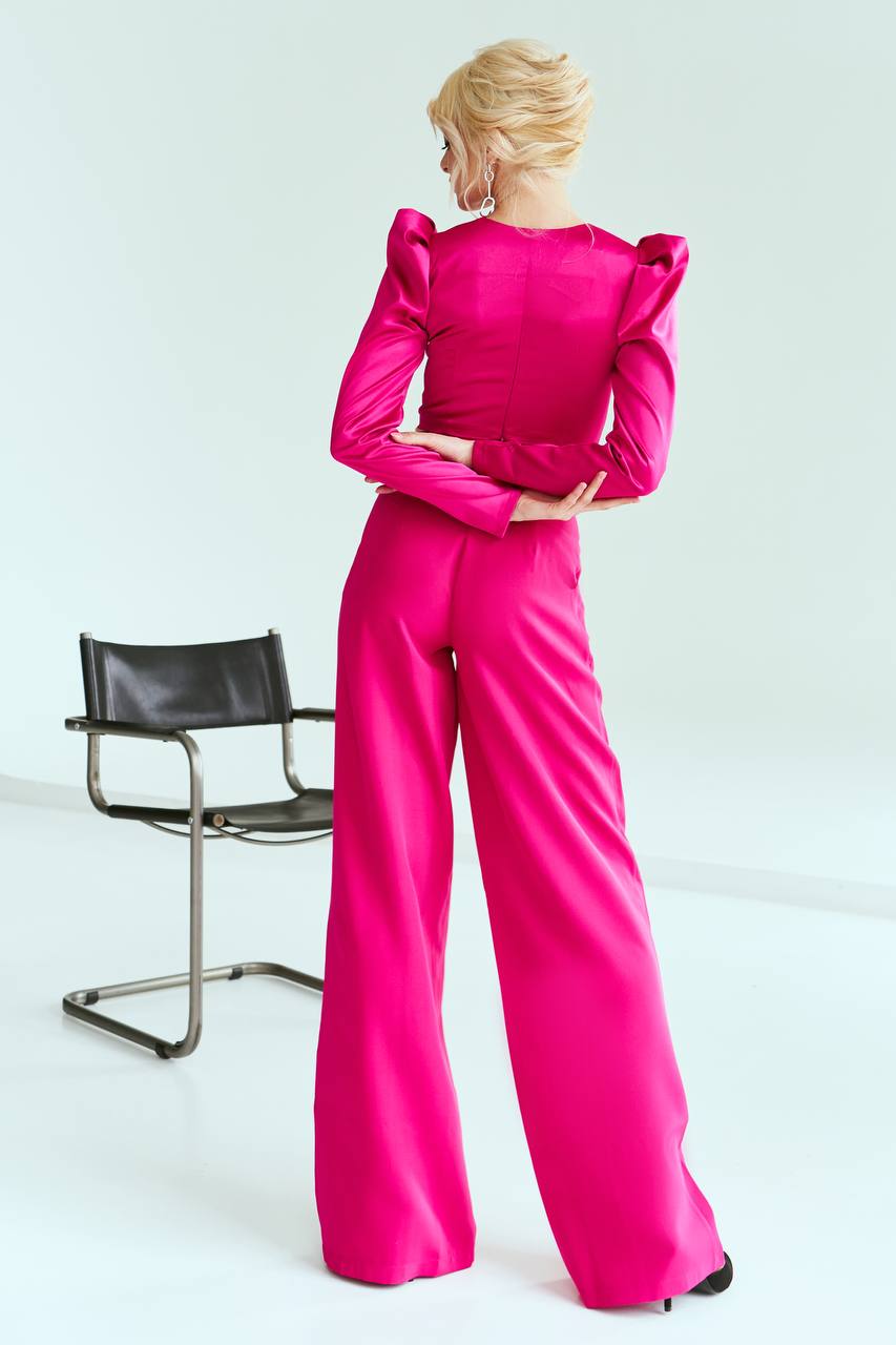 Person wearing a bright pink outfit standing in front of a black chair on a white background