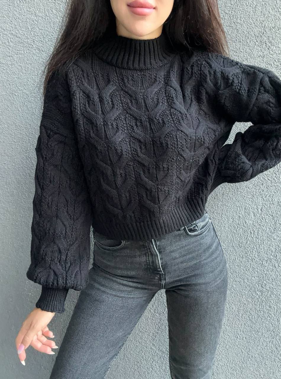 Person wearing a dark gray cable knit sweater and jeans against a plain background