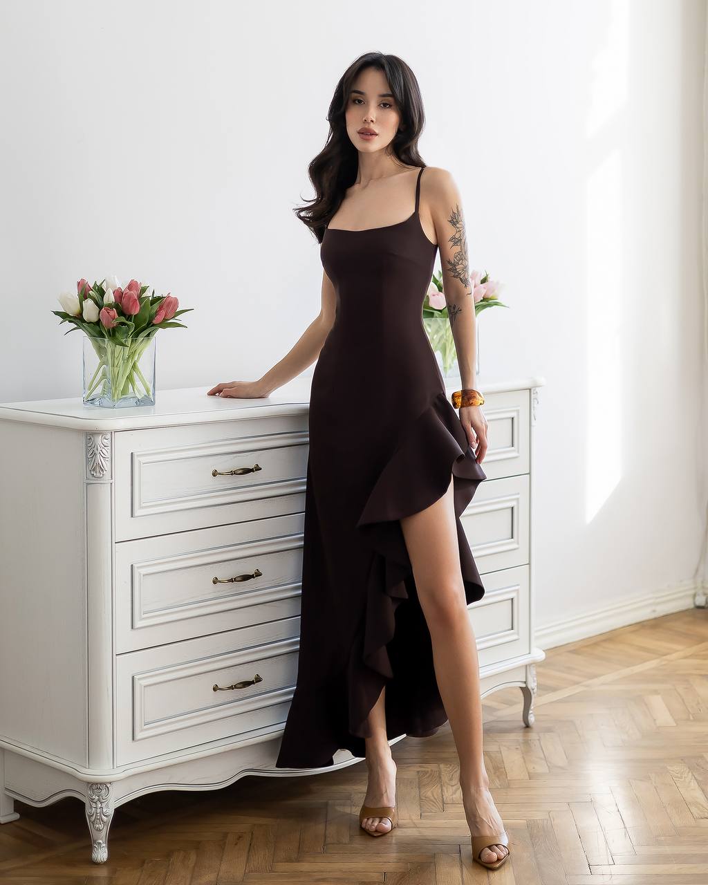 Woman in a black dress standing in a room with white furniture and flowers.