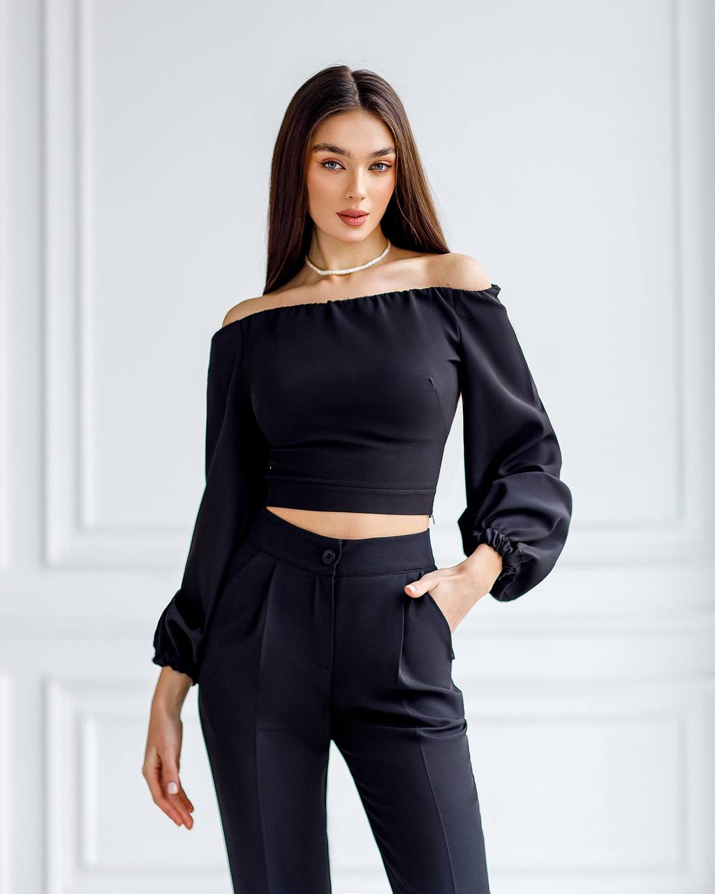Woman wearing a black off-shoulder top and black pants against a white background
